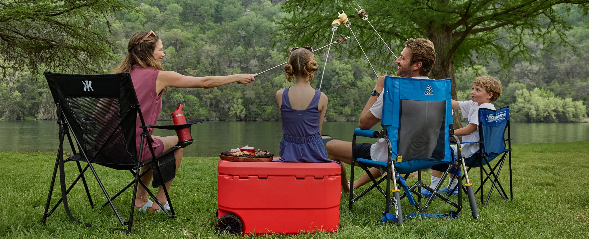 Family roasting marshmallows by lakeside in chairs