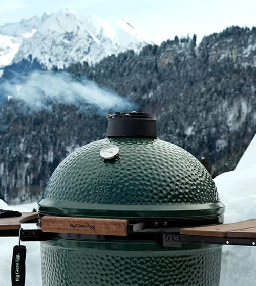 Big Green Egg grill with snow covered mountains in the distance.