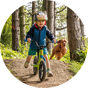 Child on a bike with a dog running next to him.