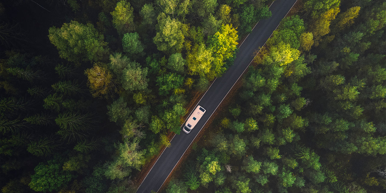 White camper van with solar panels drive through green forest