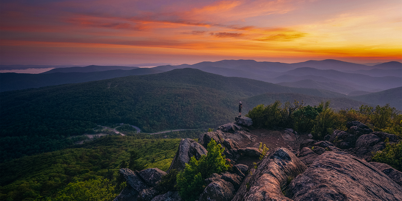 A hiker at the summit of Mary's Rock taking in a gorgeous Summer sunrise in Shenandoah National Park.