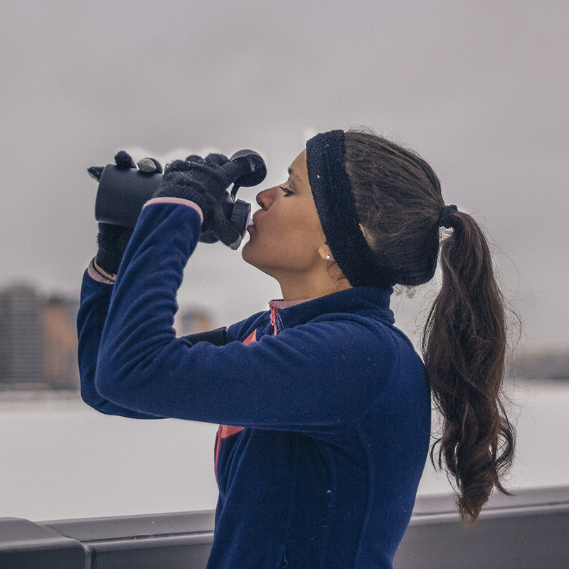 A woman drinks water outside on a cloudy winter day