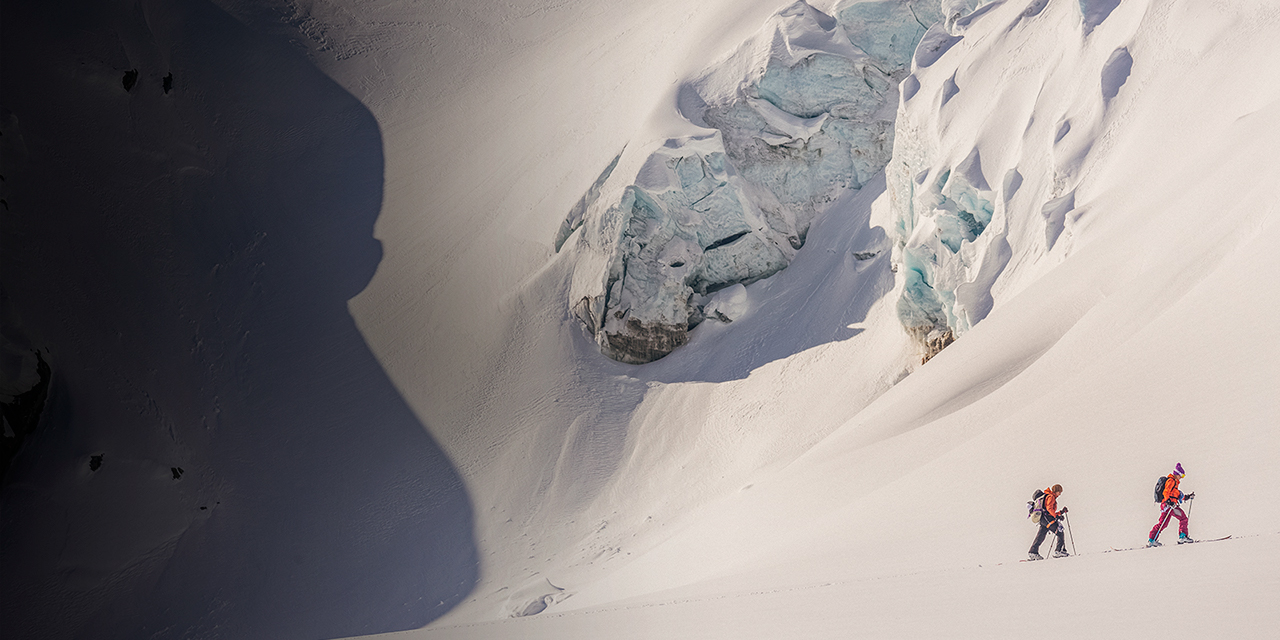 Backountry women skiers skinning up hill in the dramatic snowy mountains of the rugged Selkirks in British Columbia.