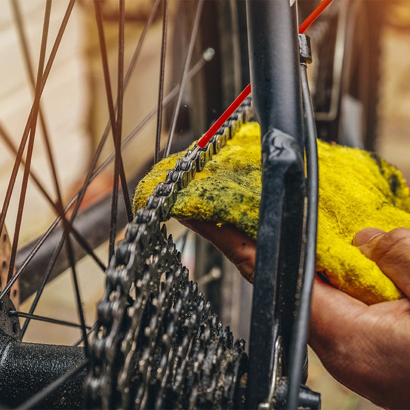 A person cleaning and oiling a mountain bike chain and gear with oil spray