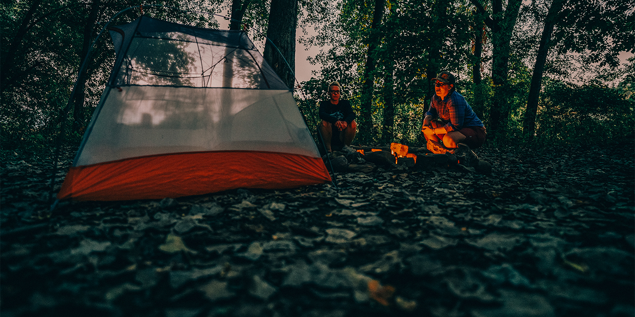 Two women sit by their tent on Sycamore Island