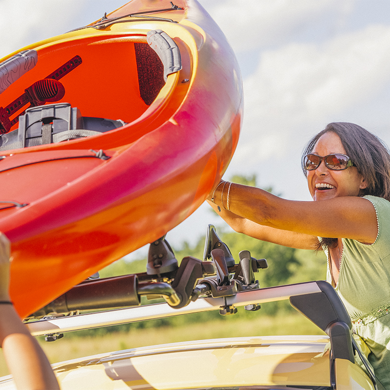 A woman puts a kayak on top of her car on a roof rack