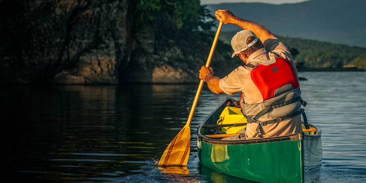 A man paddles a canoe at sunset on Lobster Lake in Northern Maine.