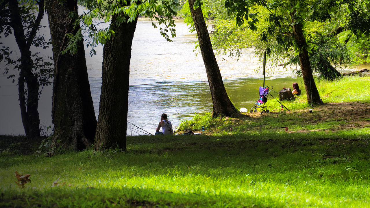 a man and a woman fishing along the Chattahoochee river surrounded by lush green grass and trees at McIntosh Reserve Park in Whitesburg Georgia