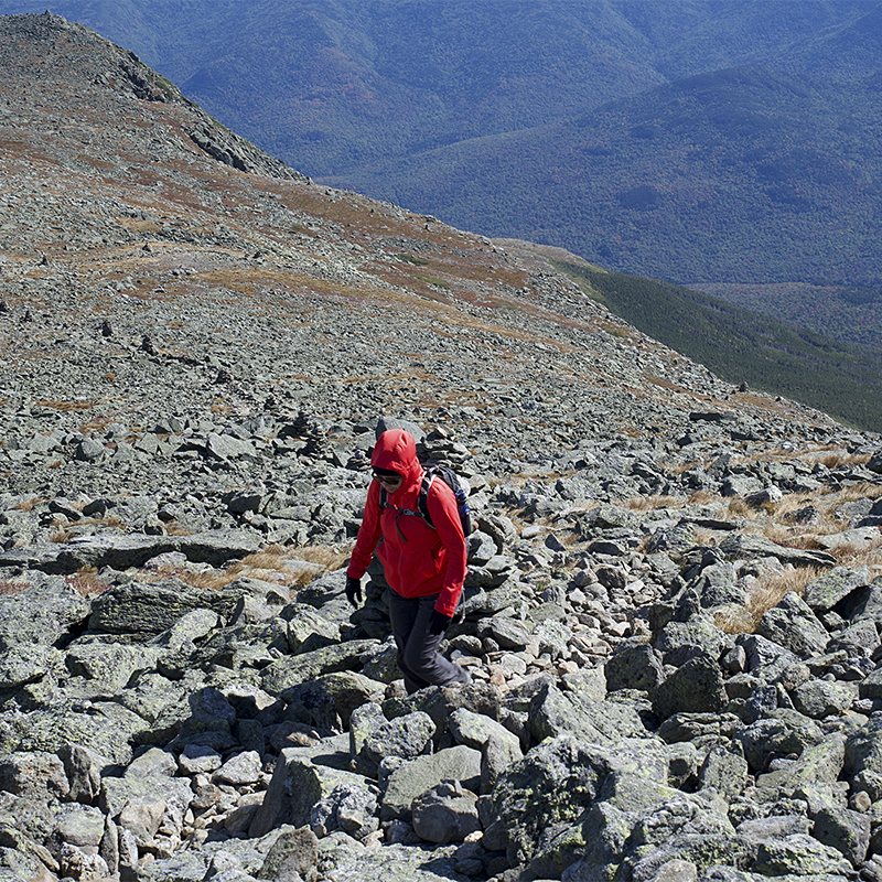 Lone hiker trekking to the summit of Mount Washington over a rocky terrain in cold windy weather