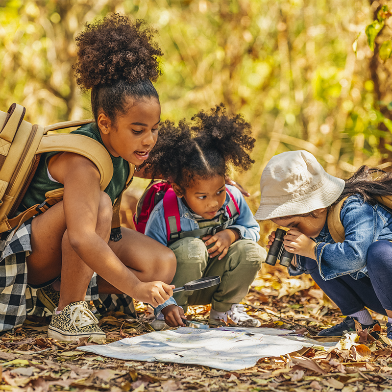 Group of  little girls hiking together with backpacks and sitting on forest dirt road with looking at the map for exploring the forest.