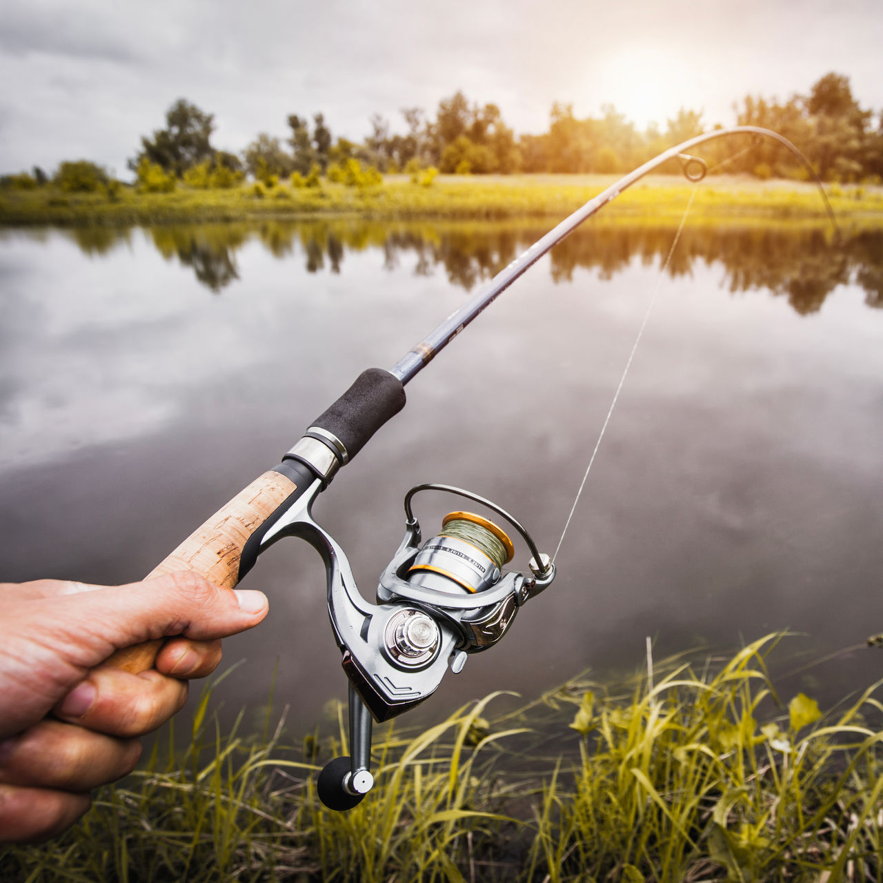 A hand with spinning and reel on the summer lake