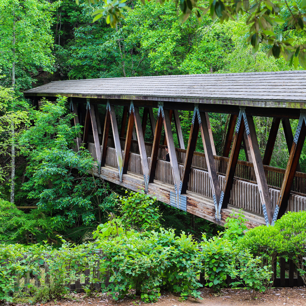 A long covered dark wood bridge over the Big Creek river surrounded by lush green lush green trees at Vickery Creek in Roswell Georgia