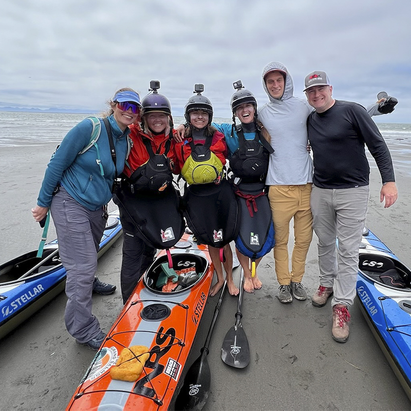 The Grand Salmon team pose in front of the ocean with kayaks