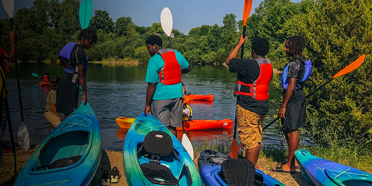 Kids stand next to kayaks with life jackets