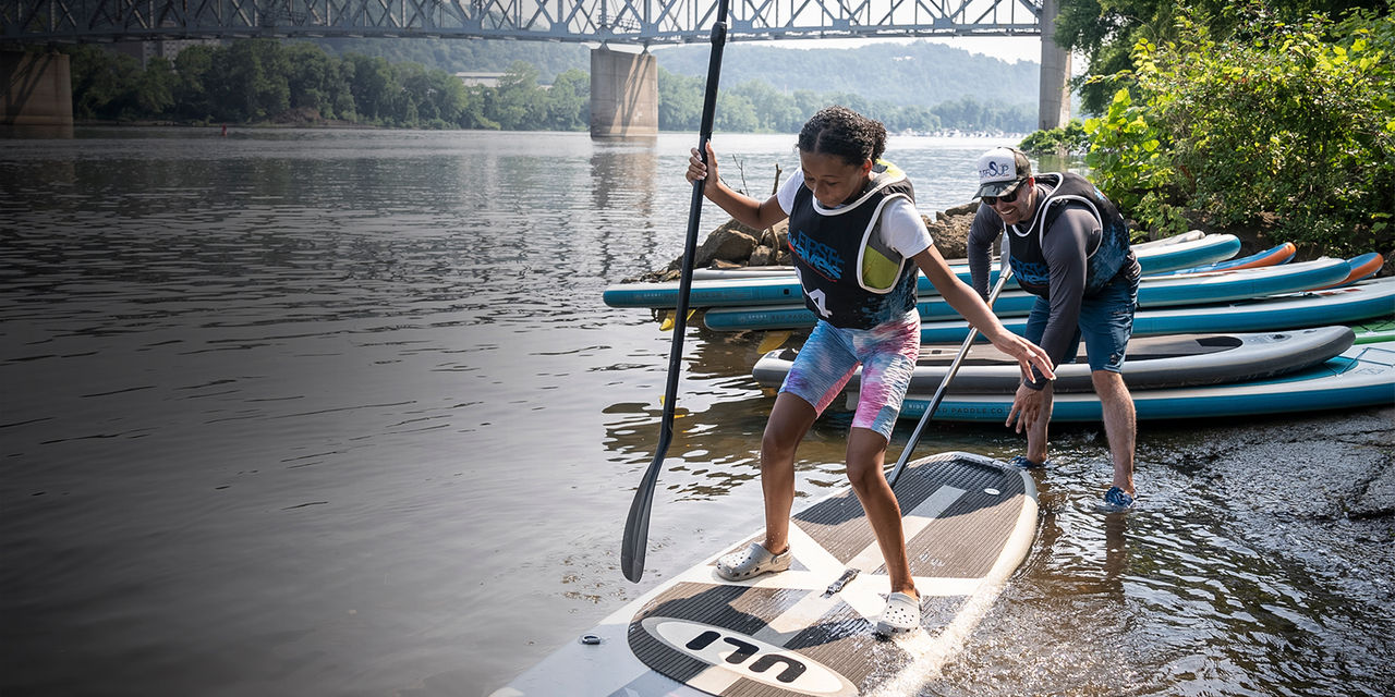 A girl stands up on a paddle board as part of First Waves