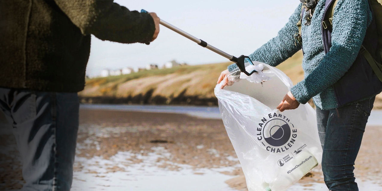 Two people pick up trash and put it in a bag on the beach