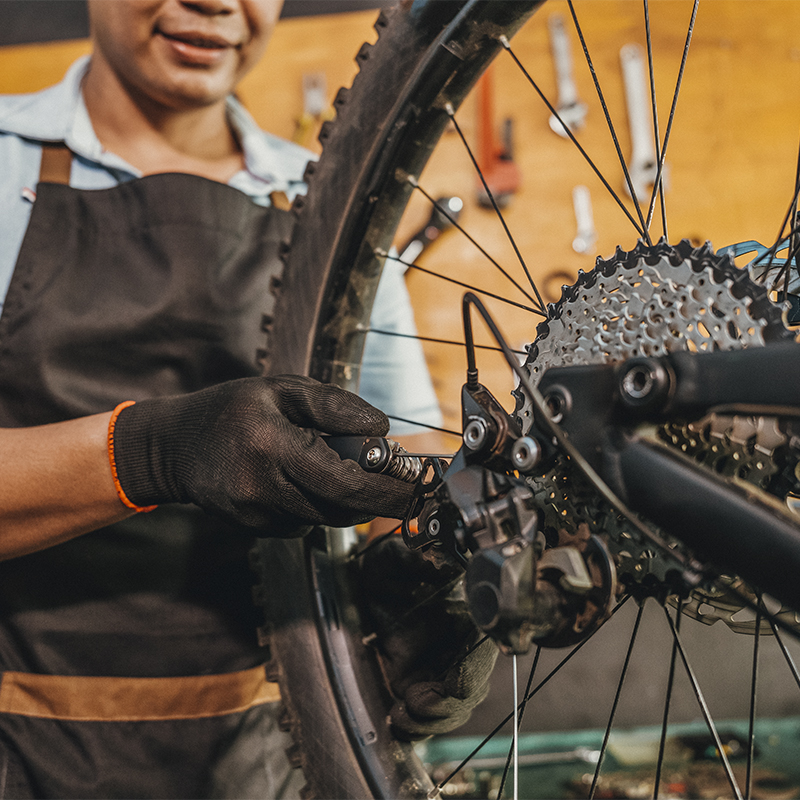 A man wearing gloves setting bicycle spoke while working in a workshop