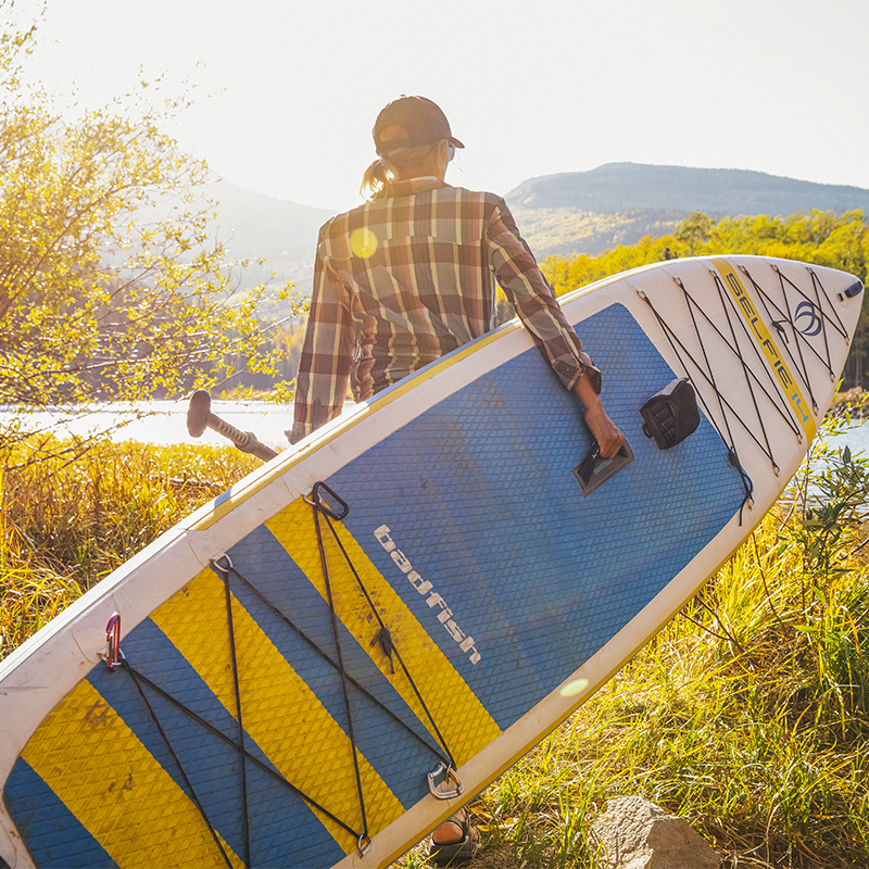 A woman carries a paddle board to the water