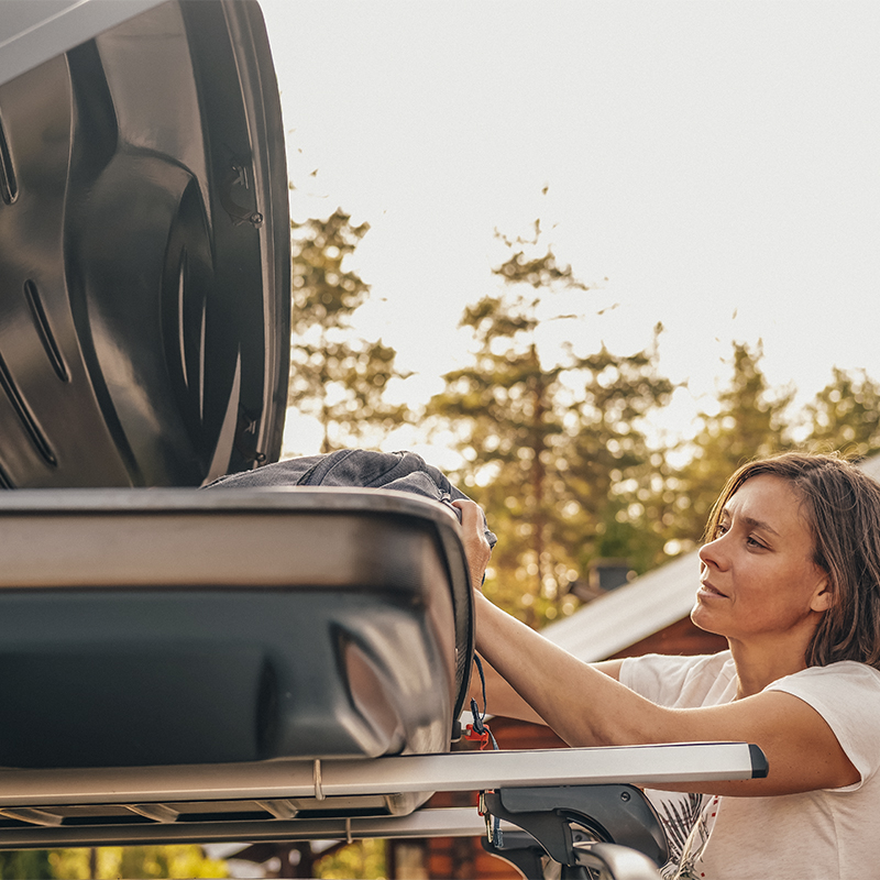 A woman puts things in the roof rack of the car