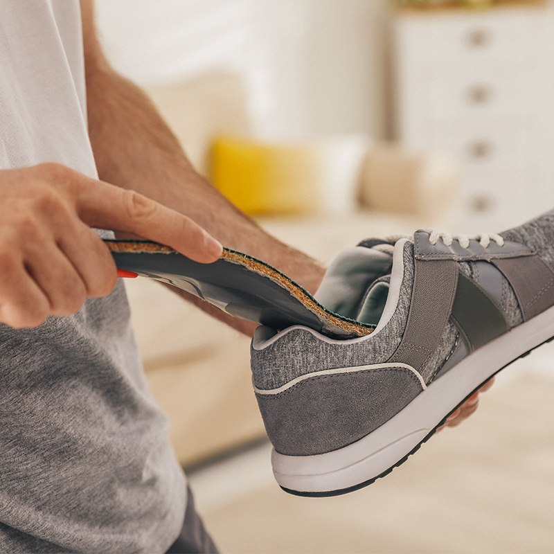 Man putting orthopedic insole into shoe at home, closeup