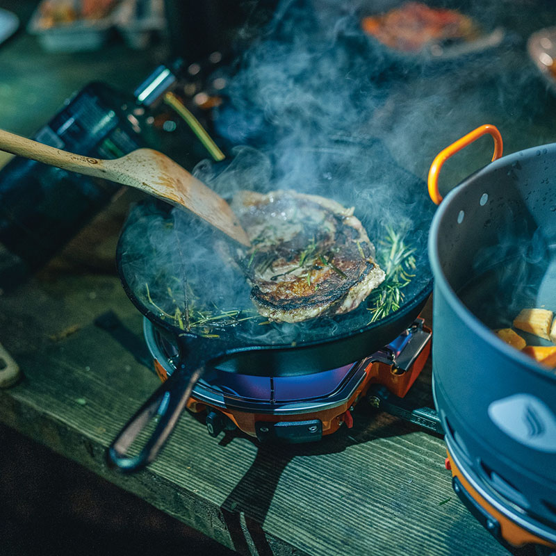 cooking a steak on a cast-iron camp stove