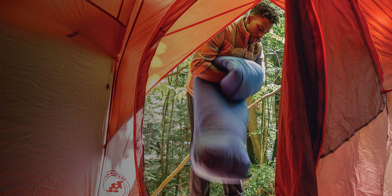 Camper rolling up sleeping bag outside of tent