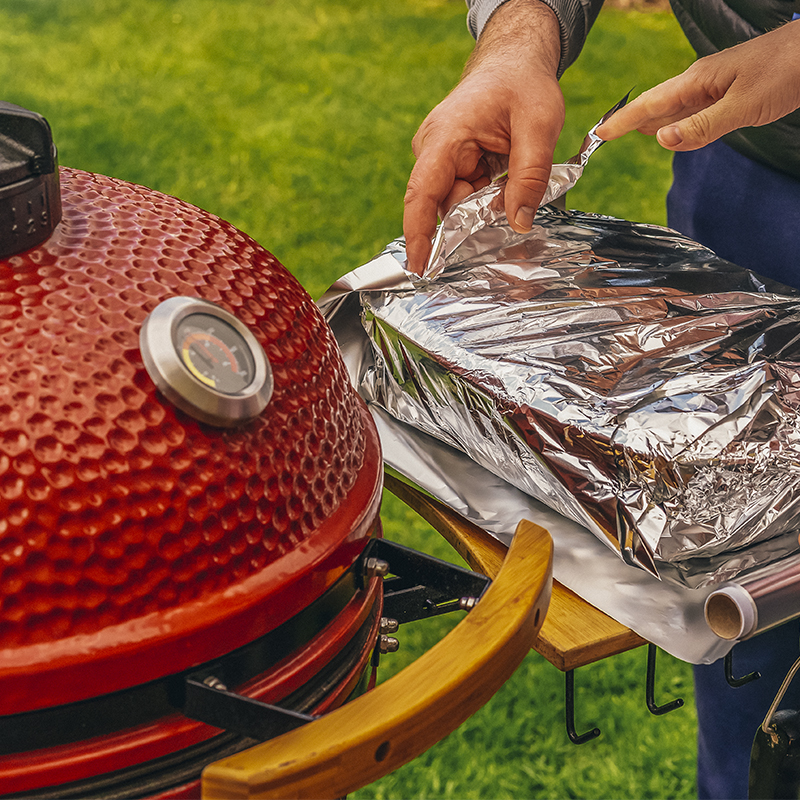 A Man and woman making food together on a red Kamado Barbecue Grill.  