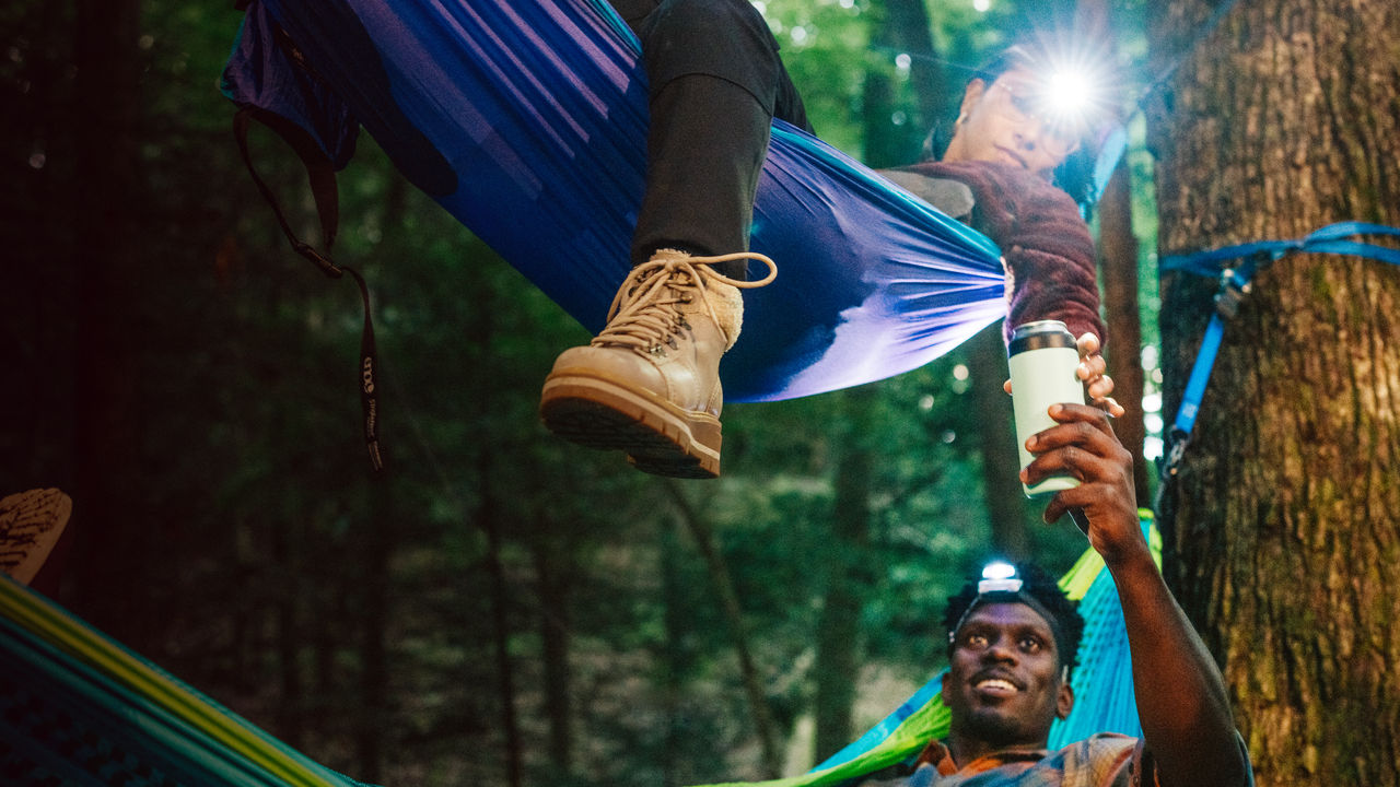 Two people lay in two hammocks and share a drink