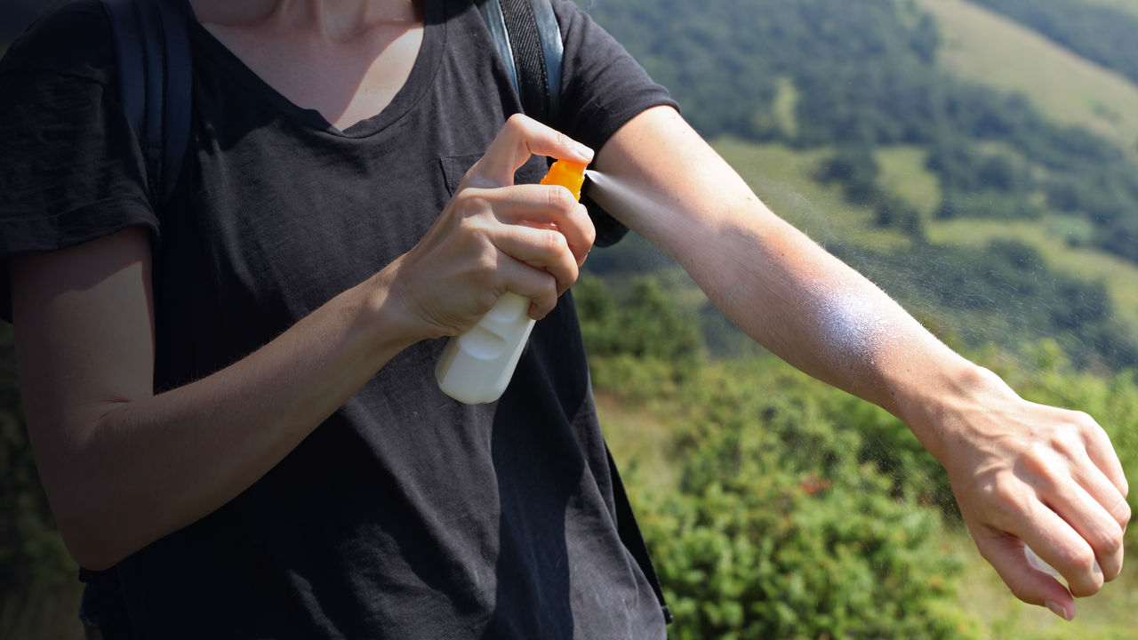 Woman hiker applying Sunscreen spray / sunblock lotion outdoors during summer hike