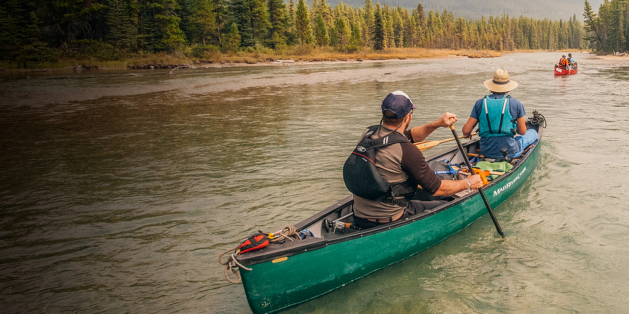 Two men canoe along the river with PFD's