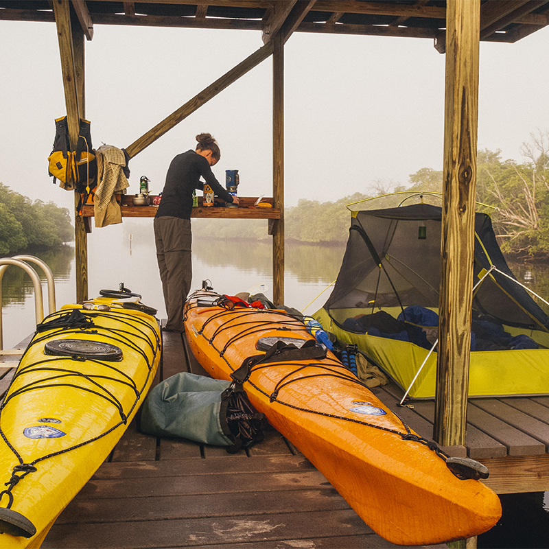 A woman makes coffee while camped on a chickee in Everglades National Park during a backcountry kayak trip.
