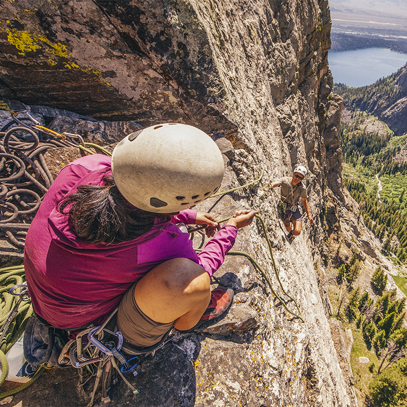 A lead climber belays a lower climber on a rockface
