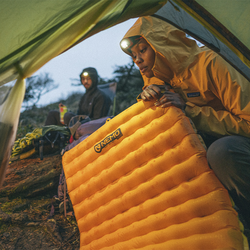 A woman blows up her sleeping pad in a tent