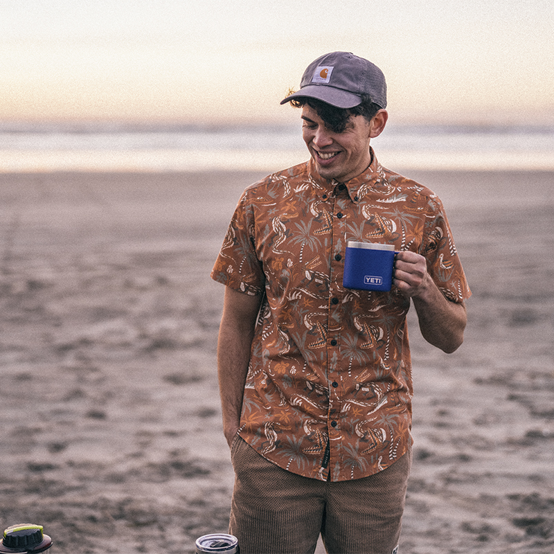A man drinks out of a camp mug on the beach