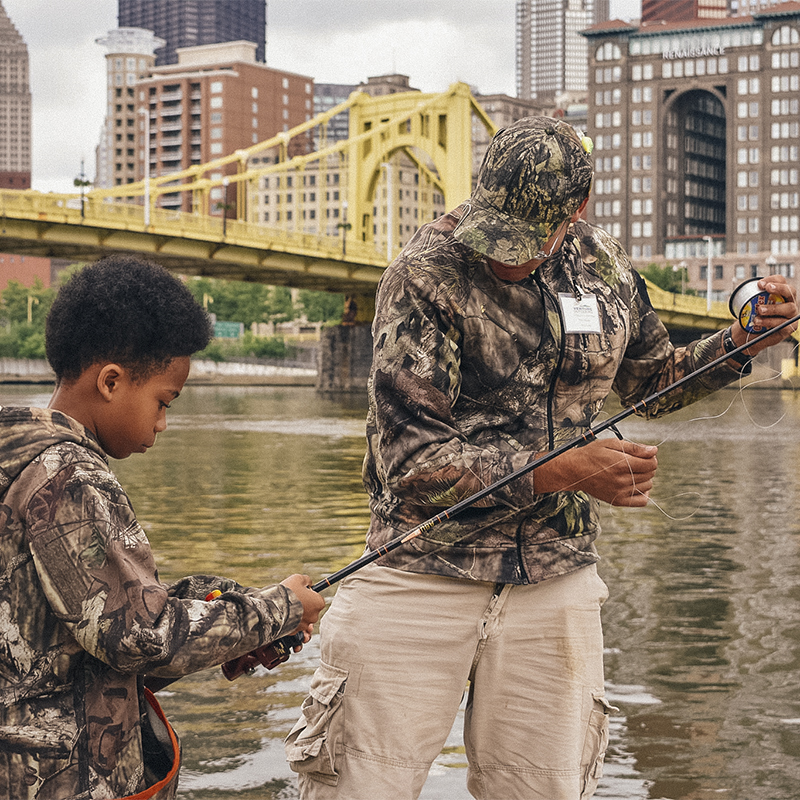 A man helps a boy fish in the river