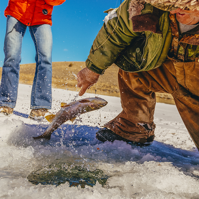 A man is teaching a woman to fish for trout on iced over Panguitch Lake, Dixie National Forest, Utah, USA