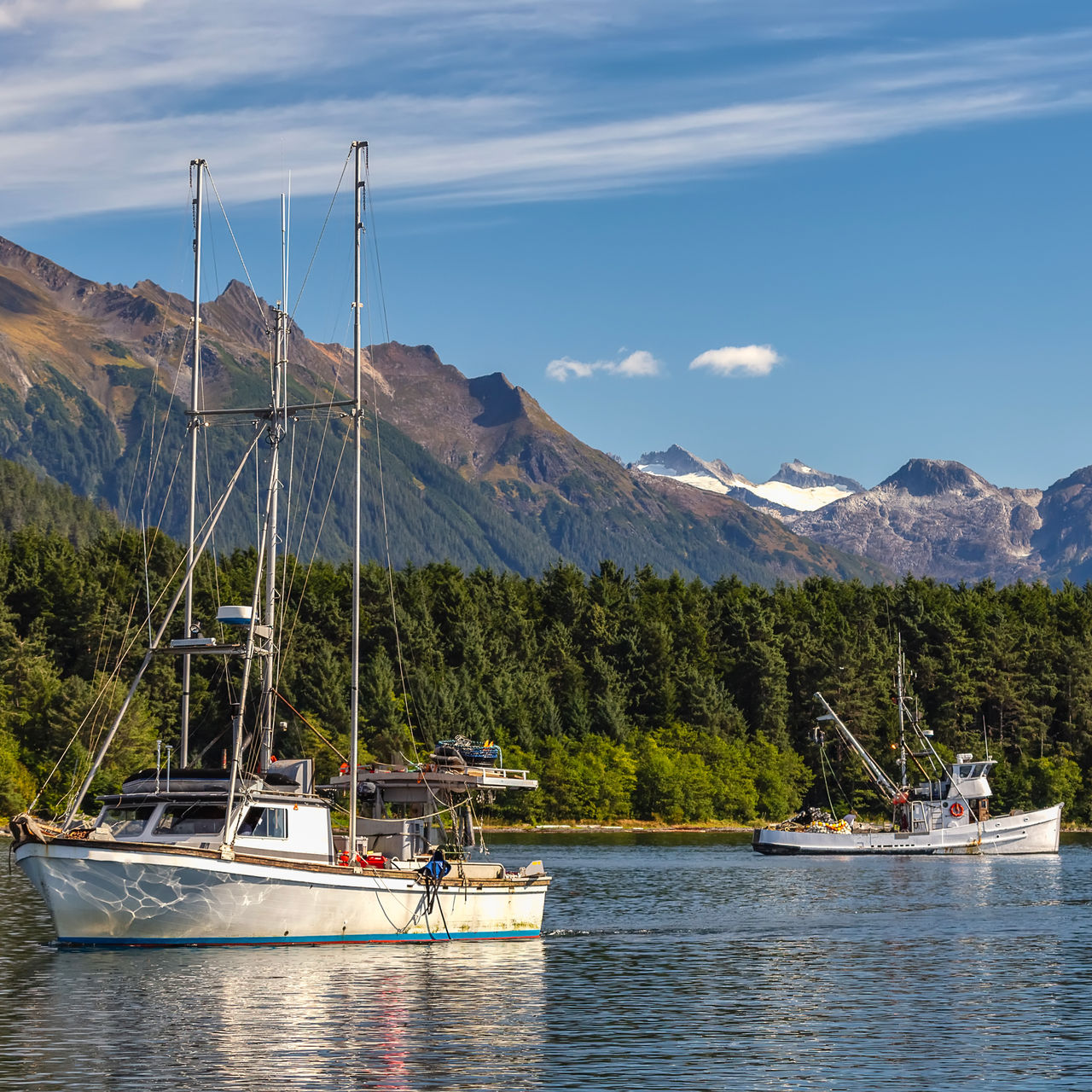 Fishing boat sailing in harbor and another fishing boat drifting behind it. Mountains, forest and blue sky in the background. Sitka, Alaska, USA, Fishing boat sailing in harbor and another fishing boat drifting