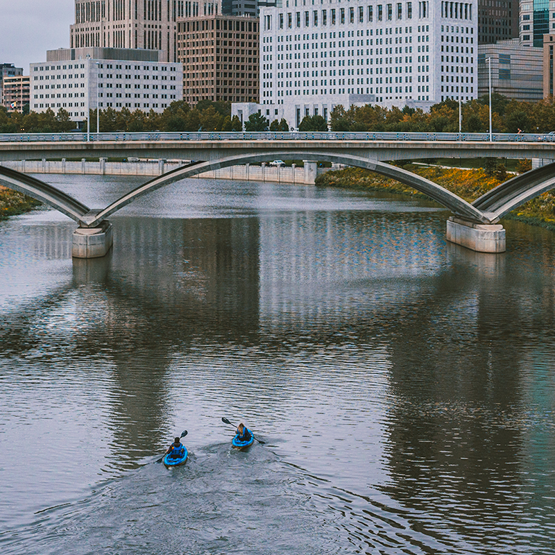 Two kayakers paddling in front of a bridge in Columbus