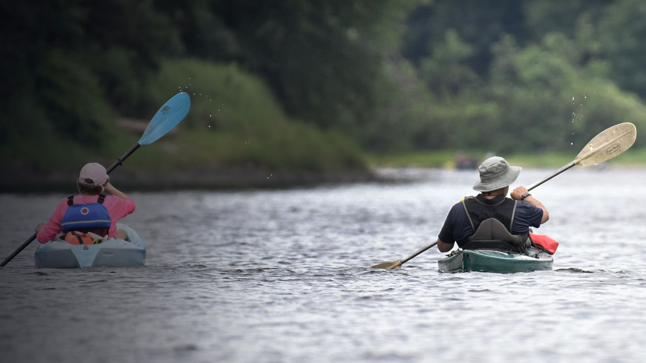 Two kayakers paddle in sync along the Delaware River.
