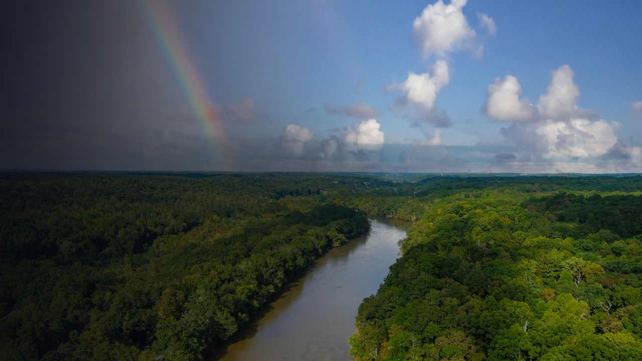 The Chattahoochee river surrounded by lush green and autumn colored trees with blue sky, a rainbow and clouds at Cochran Shoals Trail in Marietta 