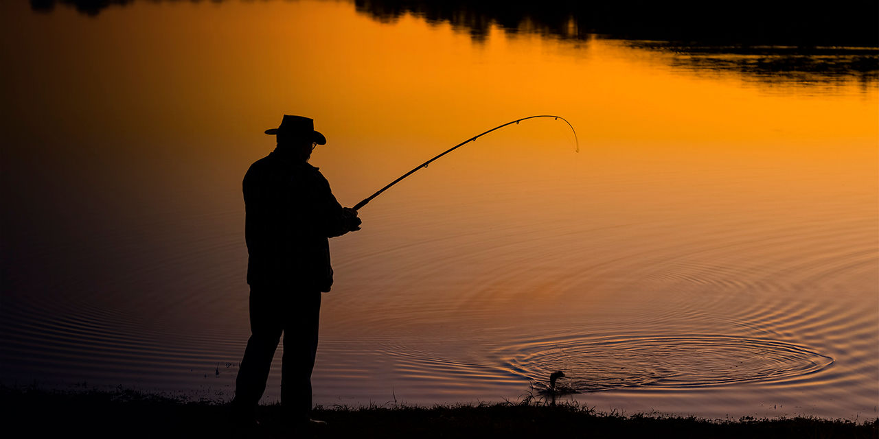 A man fishing from the shore at sunset