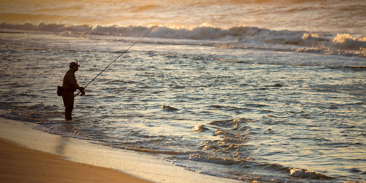 Fisherman at sea fishing during a colorful sunrise at the beach in Robert Moses State Park, Long Island, New York
