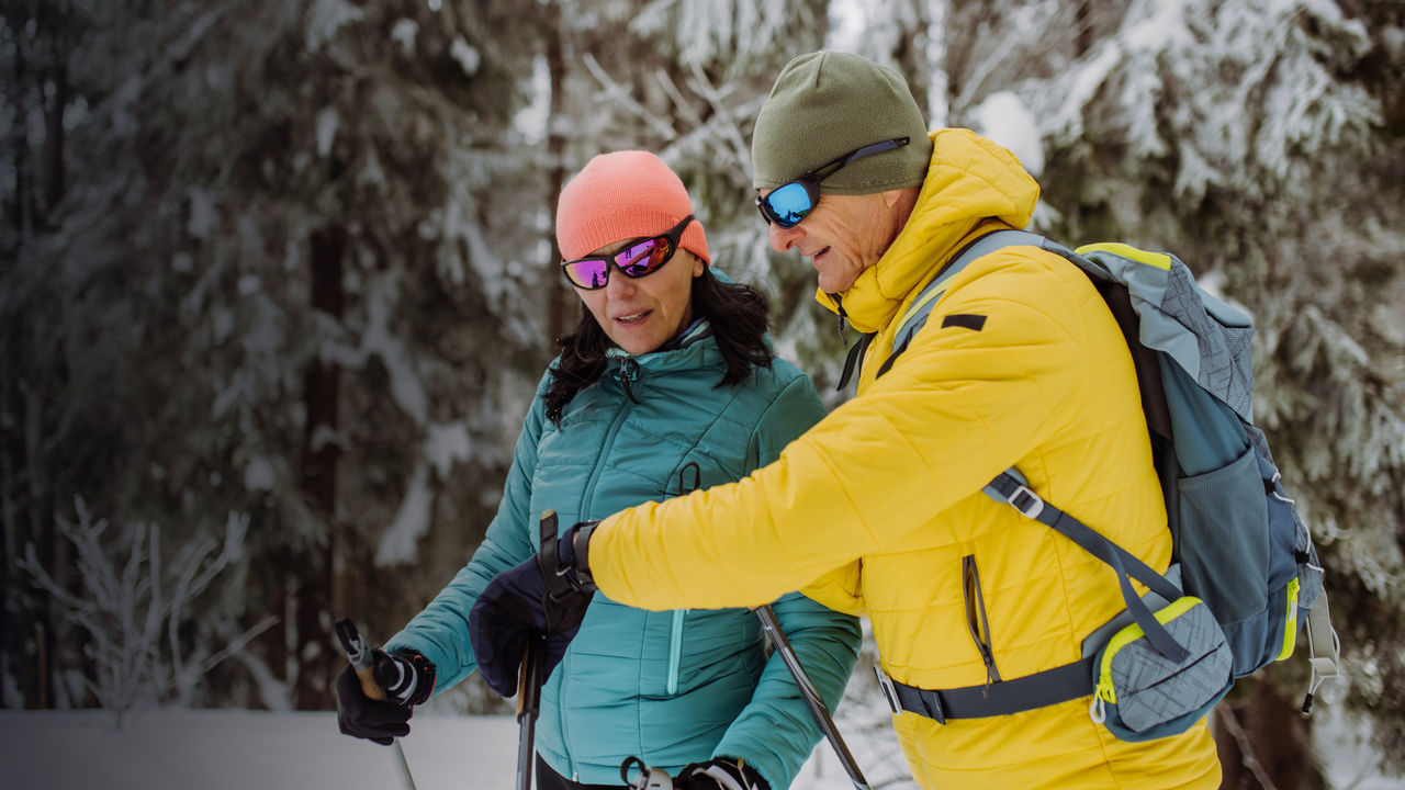 Senior couple checking smartwatch during winter skiing.