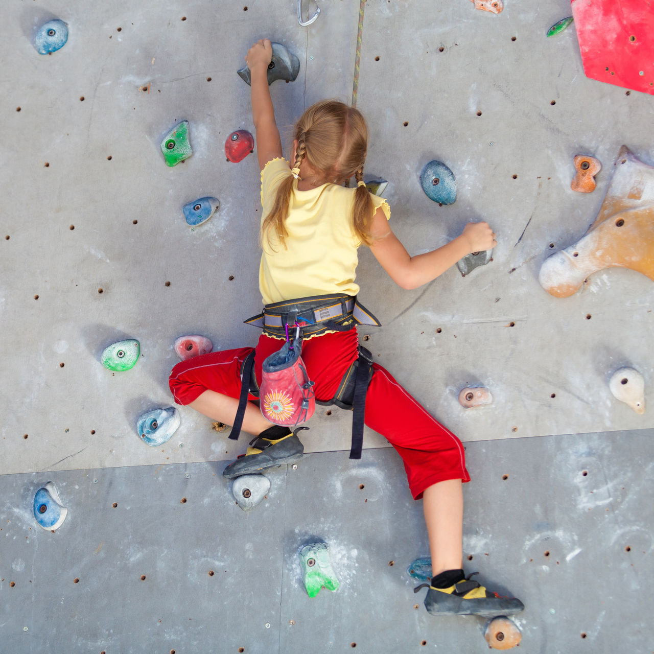 A little girl climbing a rock wall indoor