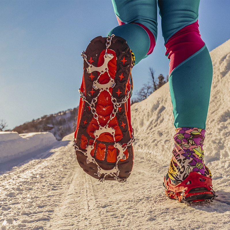 Low angle view of the bottom of trail runner's shoes with microspikes on snow covered trail. Park City, UT