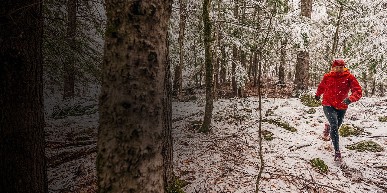 Woman in a red jacket trail running in the snow.