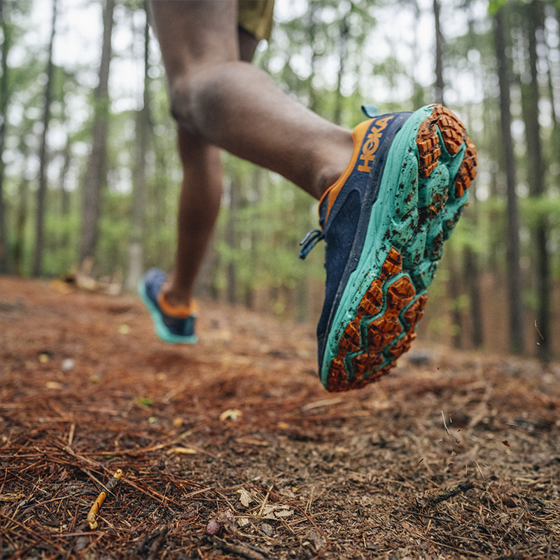 A shoe detail of a trail runner along a wooded path