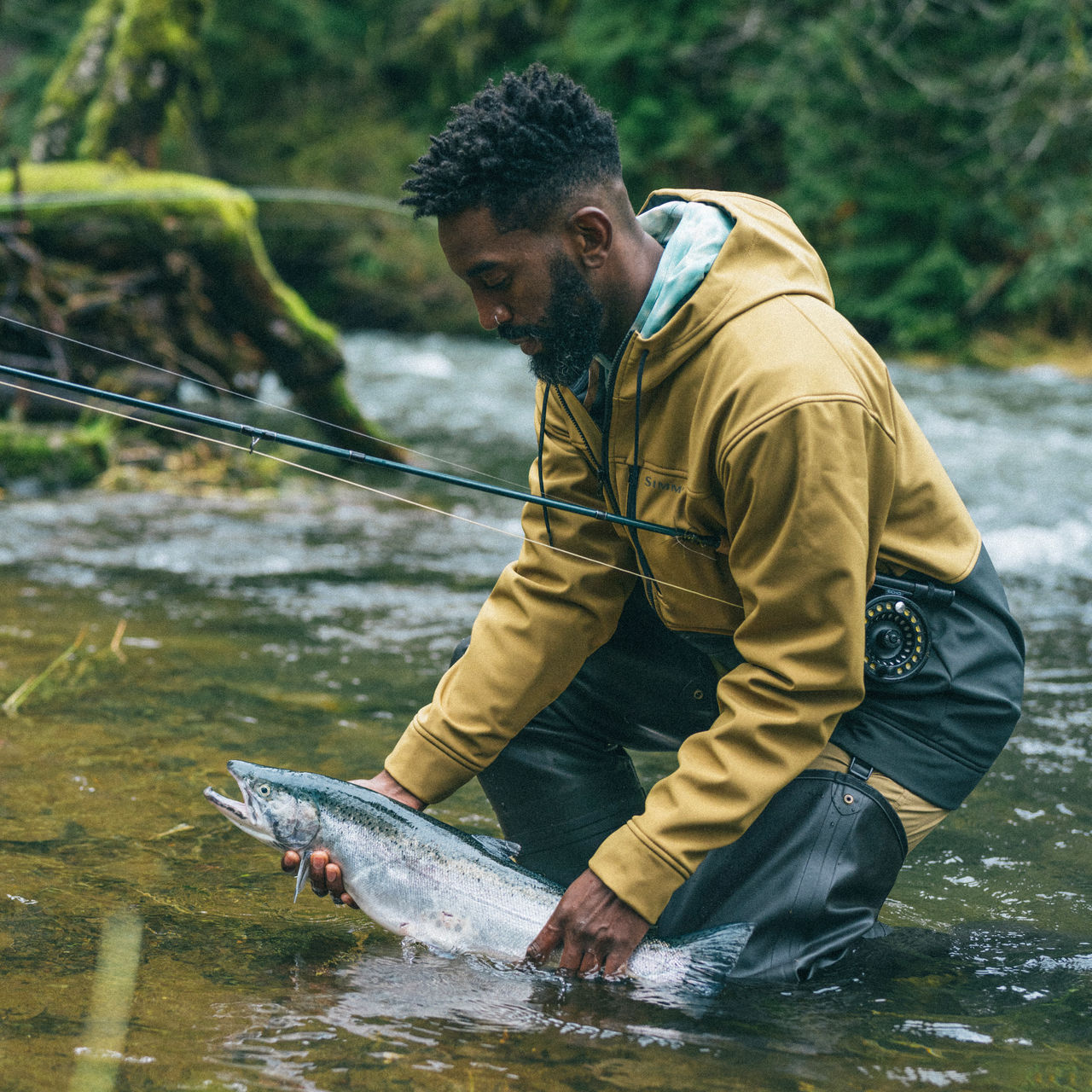 A man fishes and holds a trout fish in the water