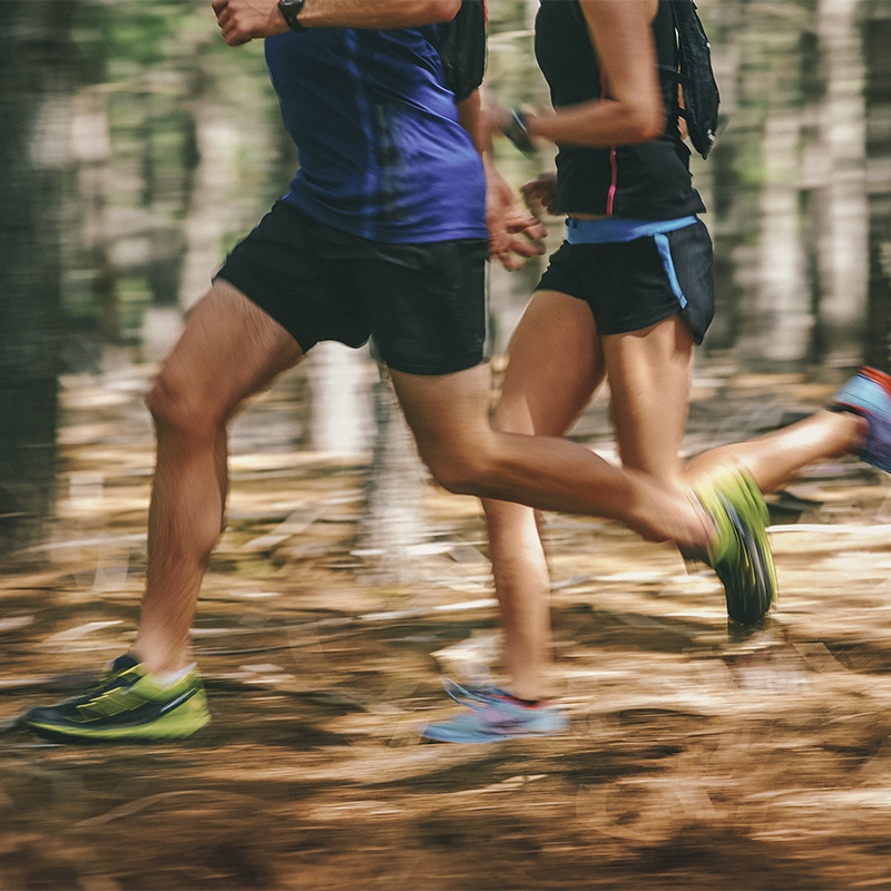 Couple running fast through the forest on trail run with motion blur