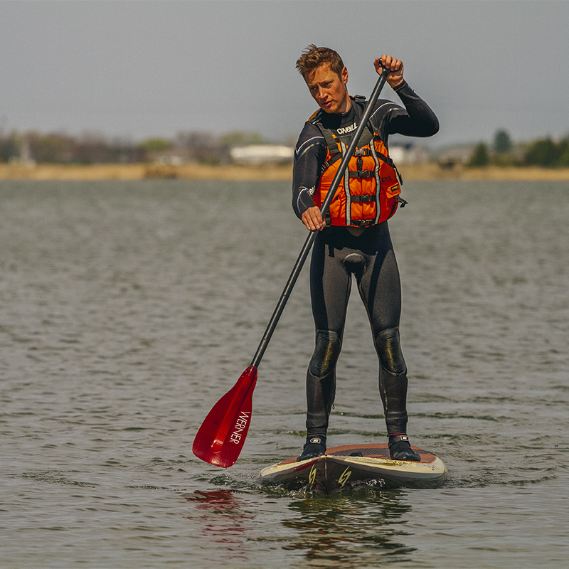A man stand-up paddle boards with a life jacket on an overcast spring day
